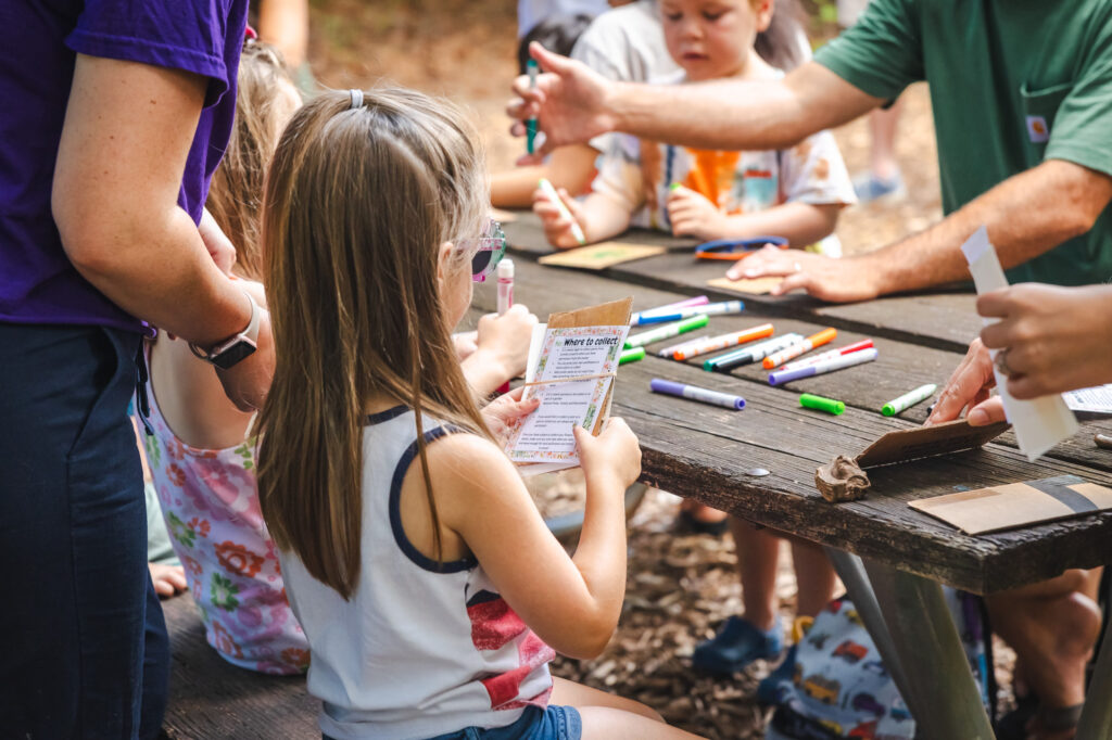 Children sitting at a wooden picnic table. They are doing the activity at Wonder Wednesday.