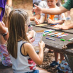 Children sitting at a wooden picnic table. They are doing the activity at Wonder Wednesday.