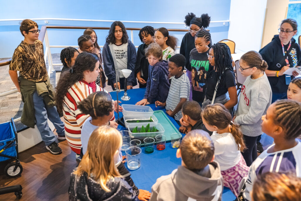Students around a table watching the indoor demonstrations about water runoff and pollution.