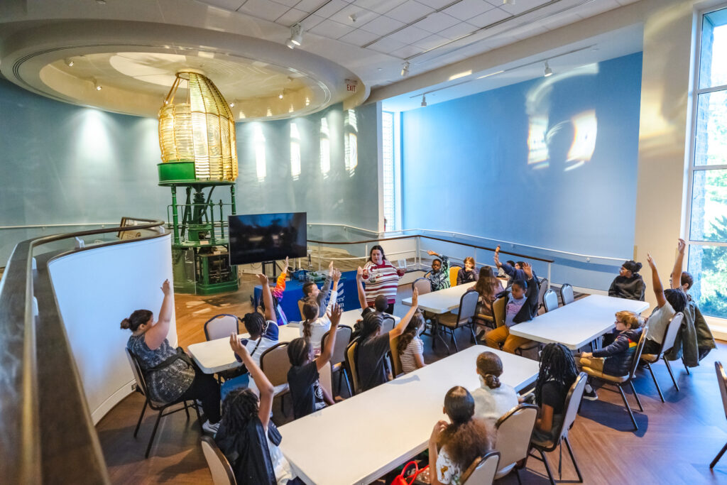 Students in the lower lobby of The Mariners' Museum raising their hands to answer a question from the educator.