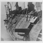 Men stand on the side of a ship that has it's cannons extended in a black and white photo